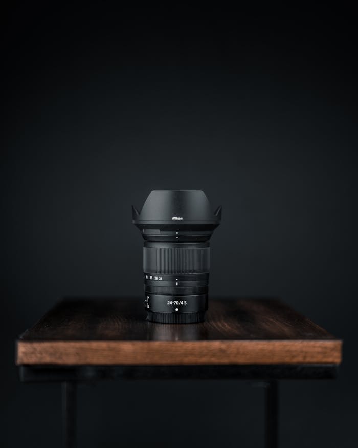 Close-up of a black camera lens on a wooden table against a dark background.